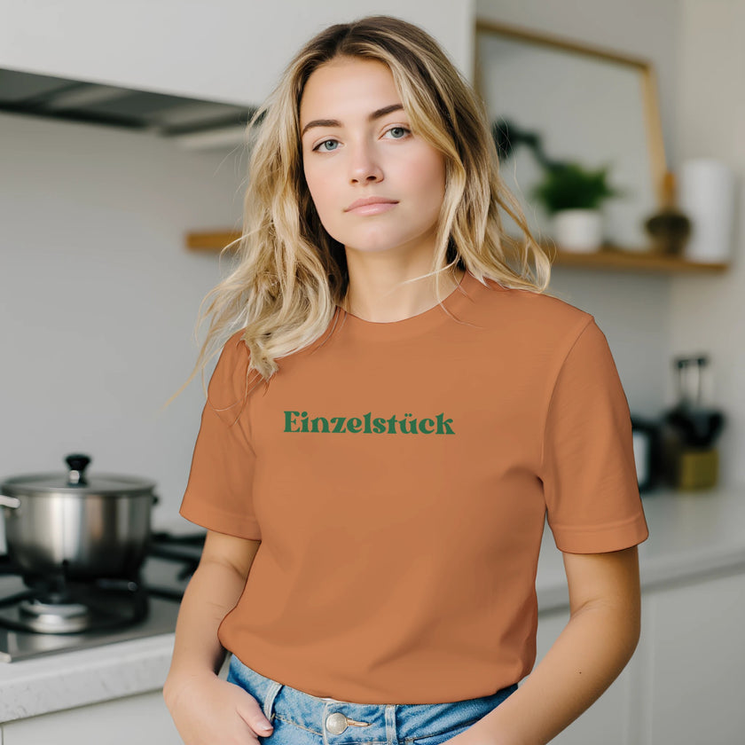 Unisex T-Shirt in gebranntem Orange aus hochwertiger Baumwolle mit grünem „Einzelstück“- Schriftzug, nachhaltig und.